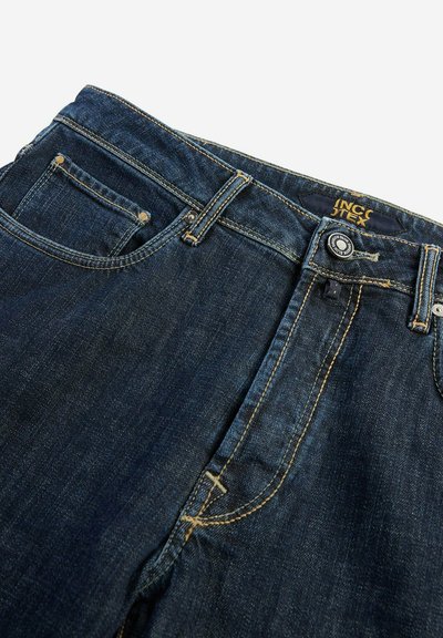 Jeans de mezclilla azul oscuro con una cintura de altura media, con costuras amarillas, diseño de cinco bolsillos y cierre de botón metálico en la parte delantera.