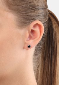 Orecchini a bottone neri con una pietra tagliata rotonda, incastonata in una base metallica. Design semplice con una superficie liscia, indossati all'orecchio di un modello.