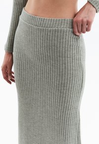 Jupe en maille ribbed de couleur gris clair, présentant une silhouette ajustée et une taille large. Texture douce avec des rayures verticales.