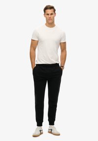 Witte t-shirt met korte mouwen, zwarte joggers en beige sneakers met zwarte accenten. De joggers hebben een elastische tailleband en boorden.