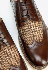 Bruine leren schoenen met een geweven stoffen bovenwerk met een houndstoothpatroon. Rond neus, vetersluiting en contrasterende texturen.