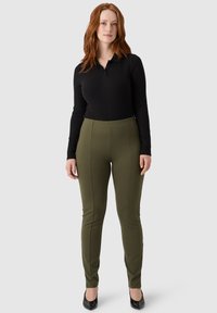 Czarna longsleeve polo z długim rękawem w połączeniu z oliwkowymi legginsami o wysokim stanie, charakteryzującymi się gładką fakturą i dopasowanym krojem. Czarne obcasy.