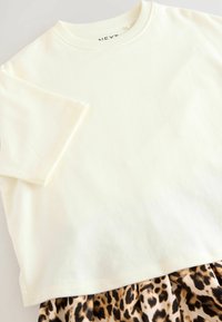 Haut en coton crème à manches courtes avec un col rond, superposé sur une jupe à imprimé léopard dans des teintes de brun et de noir.