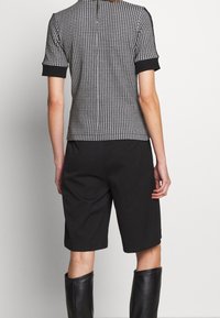 Sort-hvid houndstooth-mønstrede top med korte ærmer, parret med sorte knælængde shorts og sorte læderknæhøje støvler.