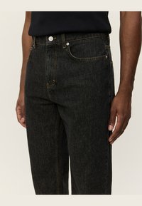 Black denim jeans featuring a straight cut, five-pocket design, contrasting stitching, and a metal button closure at the waistband.