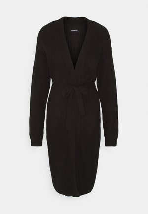 Black knitted cardigan with a deep V-neck, long sleeves, and a tie belt at the waist. Features a textured fabric and a knee-length design.