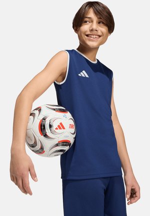 Jeune personne en tenue de sport bleue sans manches tenant un ballon de football Adidas blanc et noir, souriant et regardant sur le côté.