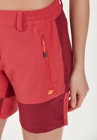 Röda och vinröda simshorts med resårmidja, dragkedjefack och en orange logotypaccent. Tillverkade av lätt, texturerad tyg.