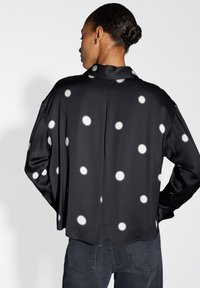 Black shirt with white polka dots, long sleeves, relaxed fit, silky texture, and a subtle vent detail at the back.