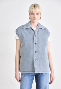 Gestreifter ärmelloser Strapazierweste aus blau-weißem Baumwollstoff, mit Kragen, knöpfbarem Vorderteil und Brusttasche, kombiniert mit Denim-Jeans.