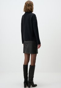 Maglione nero a maglia con collo alto, abbinato a una mini gonna di pelle nera e stivali neri fino al ginocchio. Tessuti lisci, design minimalista.