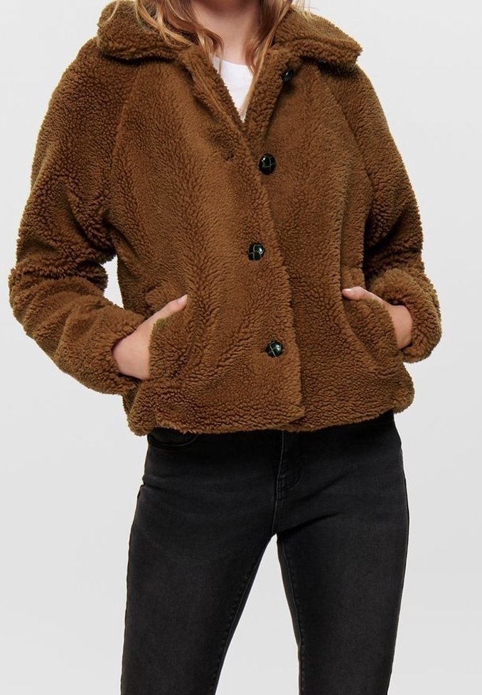 Brun, fluffig fleecjacka med krage, fyra stora svarta knappar och två sidofickor, tillsammans med mörka jeans.