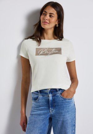 T-shirt blanc à manches courtes avec un design graphique textuel rectangulaire marron. Assorti à un jean en denim bleu clair, présentant une texture usée.