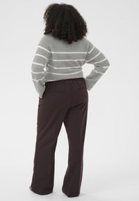 Sivý pruhovaný sveter s voľným strihom a dlhými rukávmi, v kombinácii s tmavohnedými širokými nohavicami s elastickým pásom a zadnými vreckami.