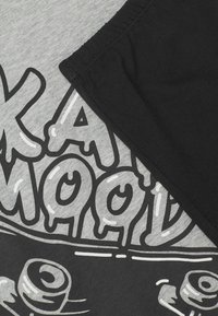 Černé a šedé tričko s velkým grafickým potiskem se stylizovaným textem a designem. Bavlněný materiál s jemnou texturou a kontrastním prošitím.