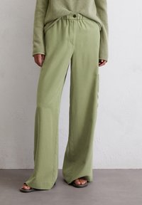 Lichtgroene wijde broek van zacht materiaal, met een elastische tailleband met een knoop, zijzakken en een relaxed fit.