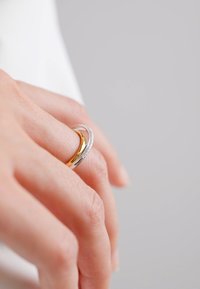 Due anelli intrecciati su una mano: uno argento con finitura testurizzata e uno oro. Linee morbide e superfici lucide creano un aspetto moderno.
