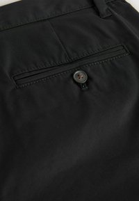 Tissu noir en gros plan montrant une poche passepoilée arrière avec un bouton foncé et des détails cousus.