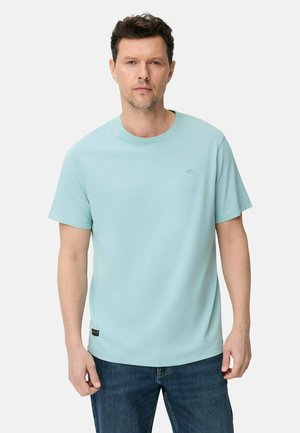 Man wearing light blue short-sleeve T-shirt and blue jeans, standing against plain light background, looking forward with neutral expression.