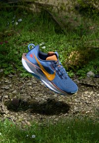 Blauwe sportschoen met een bovenwerk van mesh, oranje accenten en een gespikkelde zool. Beschikt over een opvallende oranje swoosh en vetersluiting.
