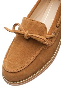 Brown suede moccasin shoe with a flat tan sole, lacing detail, and white stitching. Smooth interior lining.