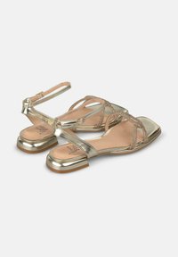 Sandales dorées métalliques à talon plat, avec plusieurs brides et un design texturé. L'intérieur est doté d'une semelle lisse beige.