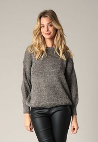 Pull en tricot gris avec texture côtelée, col rond et manches ballon. Associé à un pantalon en cuir noir pour un look décontracté.