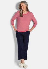 Leichter, gestreifter Pullover in Rosa und Weiß, mit Dreiviertelärmeln und gerippten Bündchen. Kombiniert mit weit geschnittenen dunklen Denim-Hosen und weißen Turnschuhen.