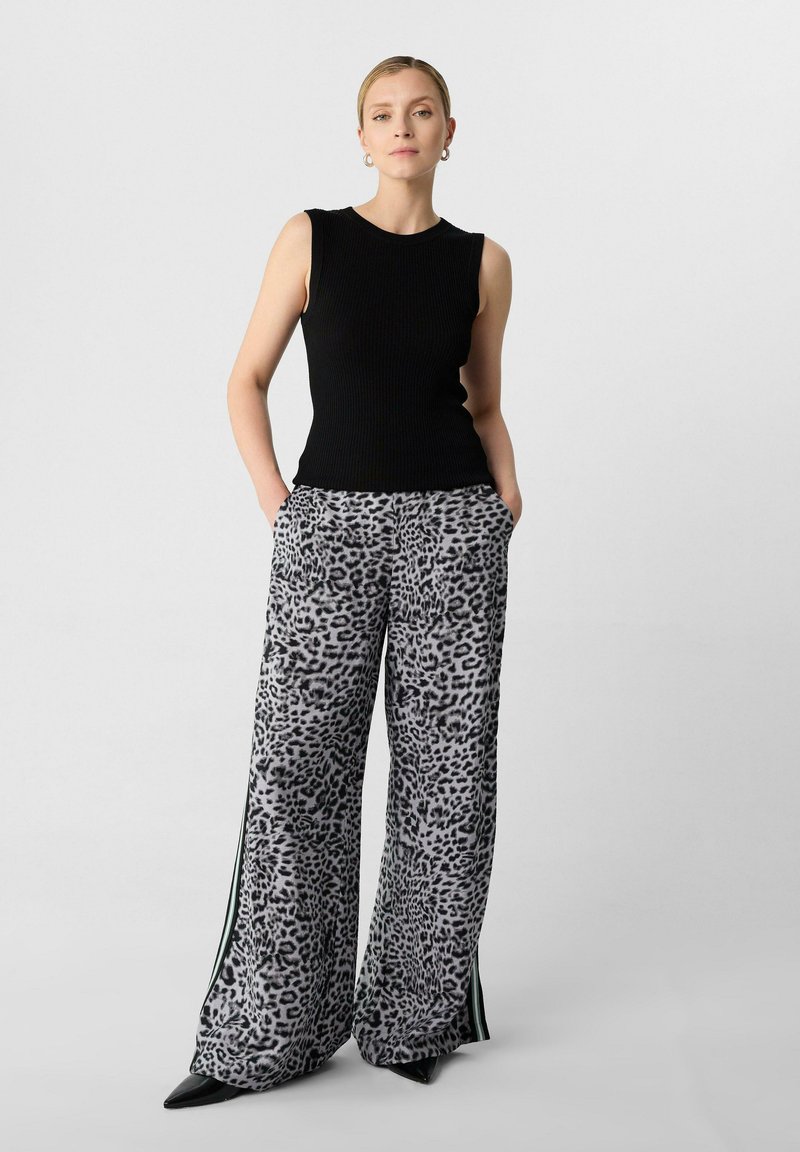 Czarny prążkowany top bez rękawów zestawiony z szerokimi spodniami w szare cętki z bocznymi pasami i kieszeniami, noszonymi z czarnymi szpilkami.