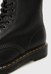 Botte en cuir noir avec une finition texturée, bout rond, surpiqûres surélevées et surpiqûres jaunes contrastantes le long de la semelle. Dotée d'œillets en métal et de lacets.