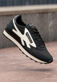 Sneaker Reebok in bianco e nero, con tomaia in suede e pelle, chiusura con lacci e suola testurizzata per una migliore aderenza.