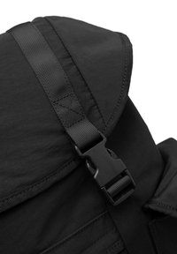 Schwarzer Rucksack mit einem umschlagbaren Deckel, der eine strukturierte Oberfläche, einen verstellbaren Webriemen und einen Plastikverschluss aufweist.