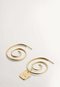 Un par de pendientes de aro en espiral dorados sobre una superficie blanca, uno de ellos con un charm dorado rectangular grabado con "VL".