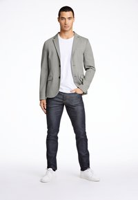 Grå kavaj över en vit t-shirt, kombinerad med mörka jeans och vita sneakers. Kavajen har slagkragar och två framfickor.