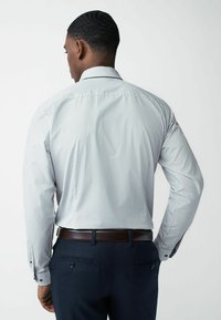 Gestreepte langekoop shirt in lichtgrijs en wit, met een button-down kraag en contrasterende manchetknopen; gedragen met donkerblauwe broeken.