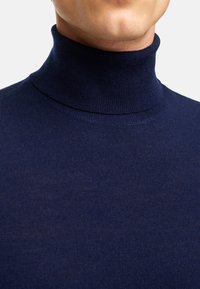 Navyblauer Rollkragenpullover mit feiner Rippstruktur, der eine tailierte Passform und einen hohen Kragen aufweist, der sich eng um den Hals schmiegt.