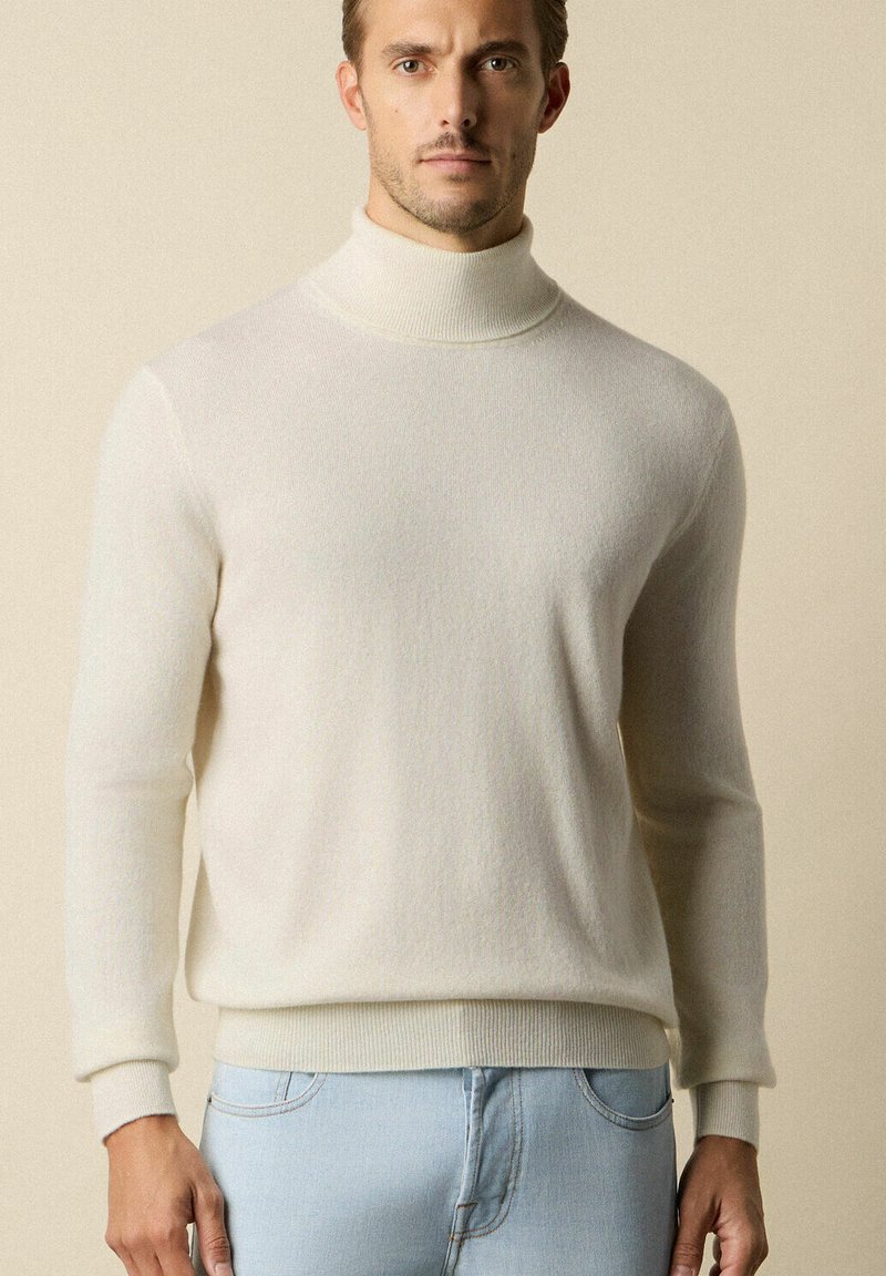 Sweter w kolorze kremowym z golfem, wykonany z miękkiej, fakturowanej dzianiny, z ribbowymi mankietami, w połączeniu z jasnoniebieskimi dżinsami. Prosty i nowoczesny design.