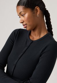 Cárdigan negro acanalado con mangas largas, escote redondo y cierre de botones en la parte delantera. Textura suave, diseño ajustado, detalles sutiles.