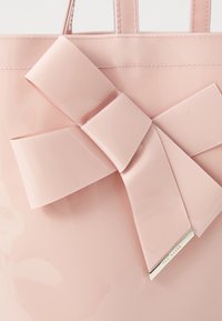 Rosa glänsande tote-väska med ett stort, slätt rosettaccent. Har en metallisk logotavla i botten. Stabil, elegant design med dubbla handtag.