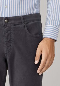 Pantalones gris oscuro de tela suave con un solo bolsillo frontal, cierre de botón y detalle de costura. Camisa a rayas azul y blanca visible.