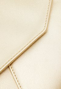 Bolso de mano metálico dorado con superficie lisa y texturizada. Presenta un cierre con solapa geométrica y costuras cuidadas a lo largo de los bordes.