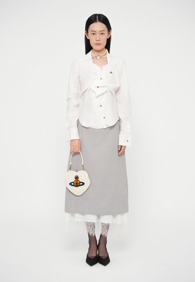 Žena má na sebe bielu košeľu na gombíky, sivú sukňu cez biele čipkové legíny, čierne topánky, perlový náhrdelník a drží bielu kabelku v tvare srdca.