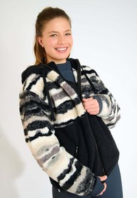 Giacca in pile con una base nera, caratterizzata da un corpo a motivo in crema, grigio e nero. Ha un cappuccio e tasche anteriori con zip.