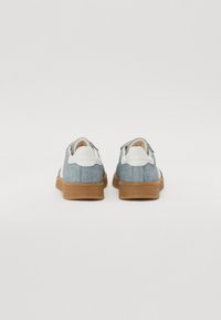 Dżinsowe trampki z jasnoniebieską cholewką z tkaniny, białym zapiętkiem i brązową gumową podeszwą z fakturowanym brzegiem. Prosty design bez wzorów.