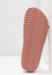 Semelle de tongs en caoutchouc rose avec un motif ondulé texturé et des bords arrondis, vue de dessous, mettant en évidence les détails de matériau et de conception.