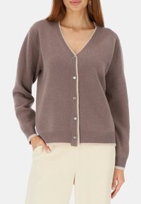 Sweter w kształcie litery V w miękkim, różowawym tkanym materiale z kontrastowymi kremowymi wykończeniami. Posiada srebrne guziki oraz prążkowane mankiety i dół, oferując luźny krój.