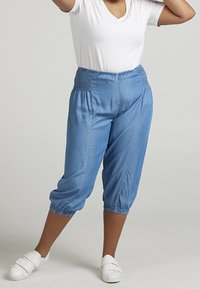 Vaaleansinisiä, chambray-tyylisiä crop-housuja, joissa on ryppyvyö ja joustavat hihnat. Yhdistetty valkoiseen V-aukkoiseen paitaan ja valkoisiin liukusandaaleihin.