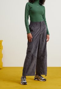 Grön långärmad topp med vita sidostrimmor, kombinerad med lösa grå cargobyxor. Byxorna har fickor och en texturerad tyg. Grå sneakers synliga.