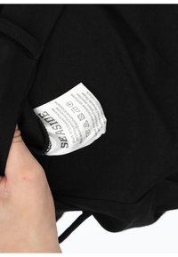 Sort tøj i sort med et plejeetiket, der viser stofsammensætning og vaskeanvisninger. Etikettet er hvidt med sort tekst.