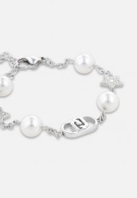 Bracelet en chaîne argentée présentant des perles blanches alternées et des accents en forme d'étoile, avec un fermoir décoratif au centre.